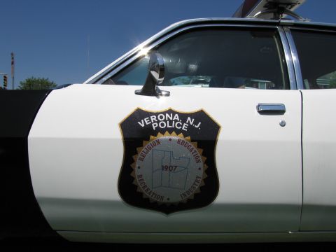 1991 Ford LTD Crown Victoria - Close-up of a black-and-white police car door showing the Verona, N.J. Police shield emblem dated 1907 against blue sky.