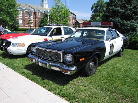 1991 Ford LTD Crown Victoria - black-and-white four-door police sedan with chrome grille and roof lightbar parked on grass among other show cruisers.