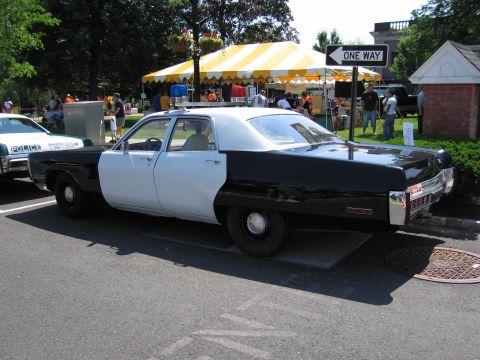 1991 Ford LTD Crown Victoria - black-and-white four-door police sedan with roof beacons parked on a street near a striped tent at a community event.