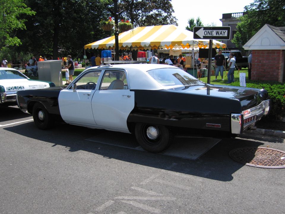 Rear three-quarter of black and white police sedan parked near a yellow tent