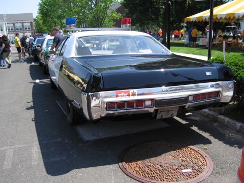 1991 Ford LTD Crown Victoria - Rear view of a black-and-white Plymouth four-door police sedan with twin red roof beacons parked among cruisers at an event.
