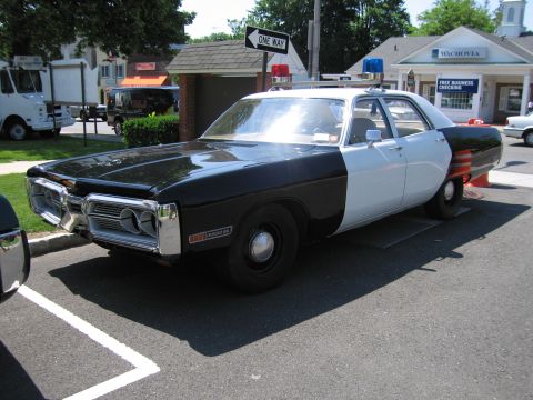 1991 Ford LTD Crown Victoria - black-and-white four-door police sedan with quad headlights parked on a street beside a One Way sign at a town show.