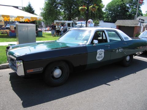 1991 Ford LTD Crown Victoria - green-and-black four-door police cruiser lettered POLICE and 9 PCT parked near festival tents at an outdoor event.