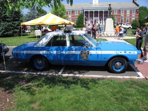 1991 Ford LTD Crown Victoria - blue NYPD '60 PCT' police sedan parked on a lawn near tents and a brick municipal building.