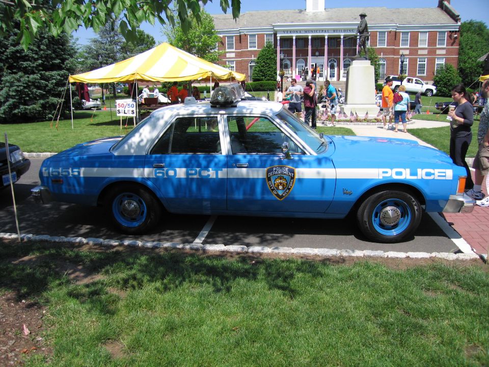 Blue NYPD 60th Precinct police sedan parked on grass at a car show
