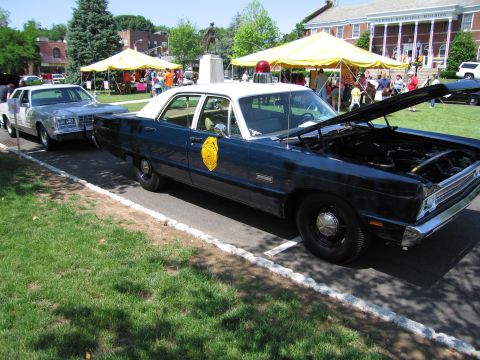 1991 Ford LTD Crown Victoria - blue-and-white vintage police sedan with a gold door emblem and raised hood, parked on grass at a car show.
