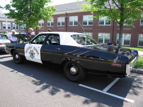 1991 Ford LTD Crown Victoria - black-and-white Highway Patrol sedan with a gold star door emblem, shown in profile near a brick building.