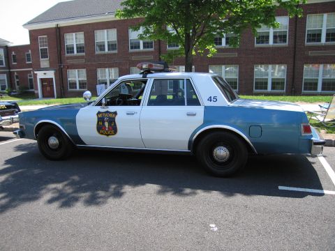 1991 Ford LTD Crown Victoria - two-tone blue Metuchen Police sedan marked '45' parked in profile near a brick building.