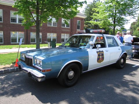 1991 Ford LTD Crown Victoria - blue-and-white Metuchen Police sedan with a roof light bar parked on a street at a car show.