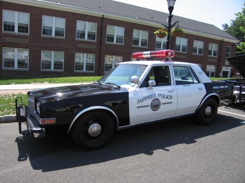 1991 Ford LTD Crown Victoria - black-and-white Jaffrey Police 'Street Crime Unit' sedan with roof light bar parked near a brick building.