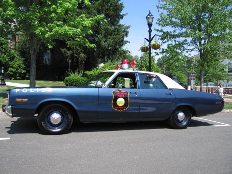 1991 Ford LTD Crown Victoria - two-tone blue-and-white vintage police sedan with a gold door emblem shown in profile under trees.