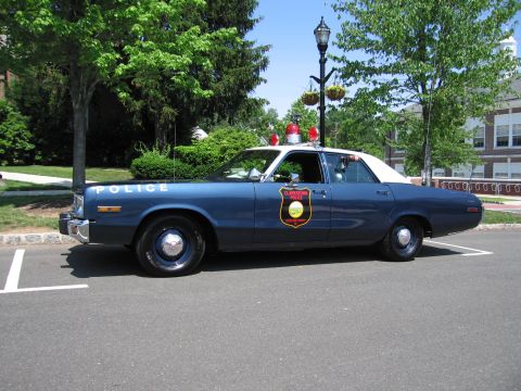 1991 Ford LTD Crown Victoria - blue police sedan with white roof and gold door emblem parked along a curb at an outdoor car show.