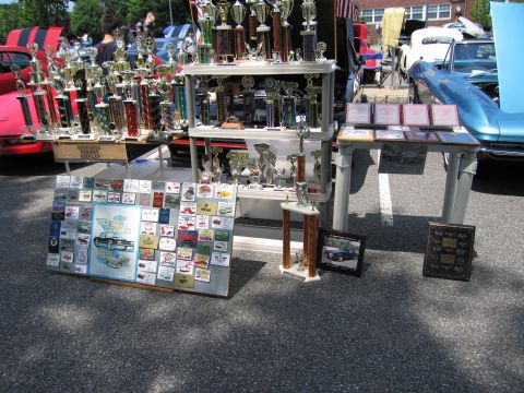 1991 Ford LTD Crown Victoria - display of car-show trophies, award plaques and photo boards arranged on tables in a parking lot.