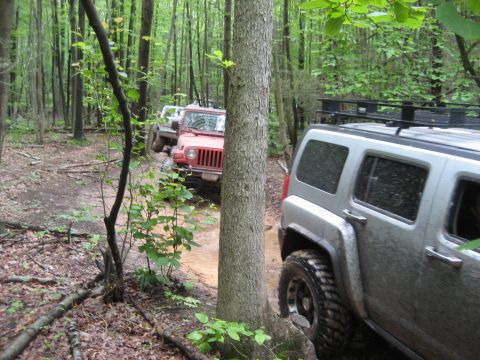 1991 Ford Bronco - Multiple off-road vehicles navigate a wet, wooded path during an event.
