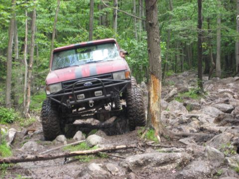 1991 Ford Bronco - This modified SUV navigates a challenging rocky and muddy path through a dense forest.
