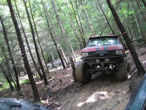 1991 Ford Bronco - Modified 1991 Ford Bronco navigates a challenging muddy path through a dense forest.