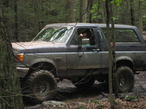 1991 Ford Bronco - A 1991 Ford Bronco navigates a challenging muddy trail in a forest setting.