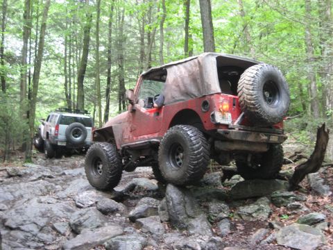 1991 Ford Bronco - Two off-road vehicles navigate a challenging rocky path through a dense forest.