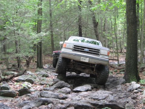 1991 Ford Bronco - A 1991 Ford Bronco navigates a challenging, rocky off-road course in a wooded area.