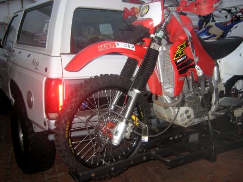 1996 Ford Bronco - A white Ford Bronco is parked with a red dirt bike loaded onto a trailer attached to its rear.
