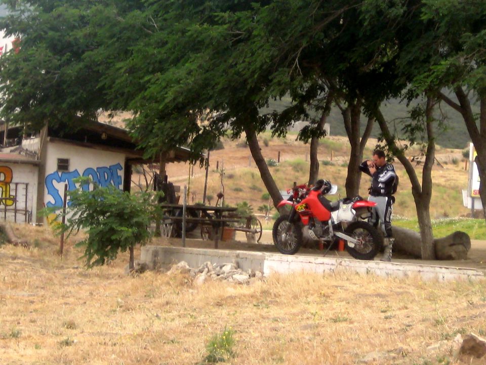 Red dirt bike parked next to a man in riding gear, with a building labeled 'STORE' in the background