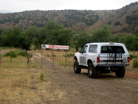 1996 Ford Bronco - A white 1996 Ford Bronco is parked on a dirt road, with a SCORE Baja 500 banner in the background.