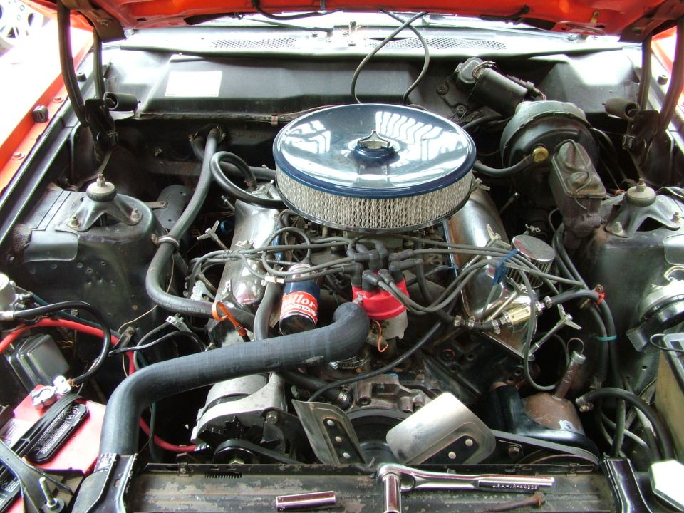 Engine bay with V8 engine, chrome air cleaner, and red distributor cap. Orange paint visible on hood