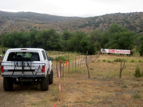1996 Ford Bronco - A white 1996 Ford Bronco is parked near a SCORE Baja 500 banner, suggesting participation in the off-road race.