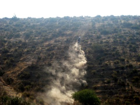 1996 Ford Bronco - A lone dirt bike ascends a dusty hillside, leaving a trail of kicked-up dirt in its wake.
