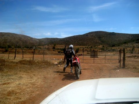 1996 Ford Bronco - A dirt bike rider pauses at a gate in a remote, arid environment under a clear blue sky.