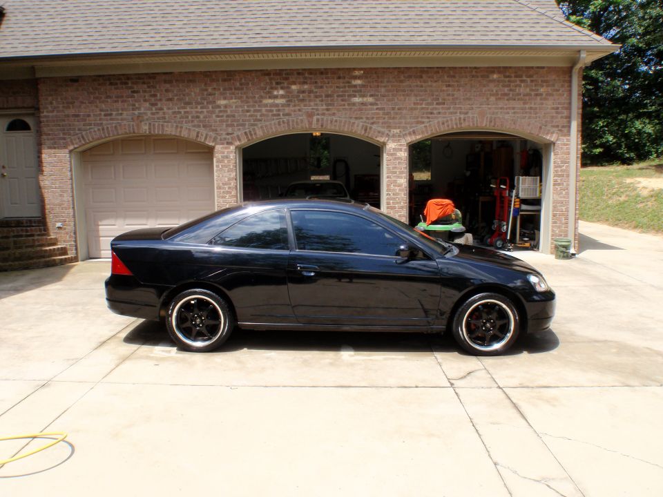 Side profile of a black Honda Civic coupe with black wheels on a driveway