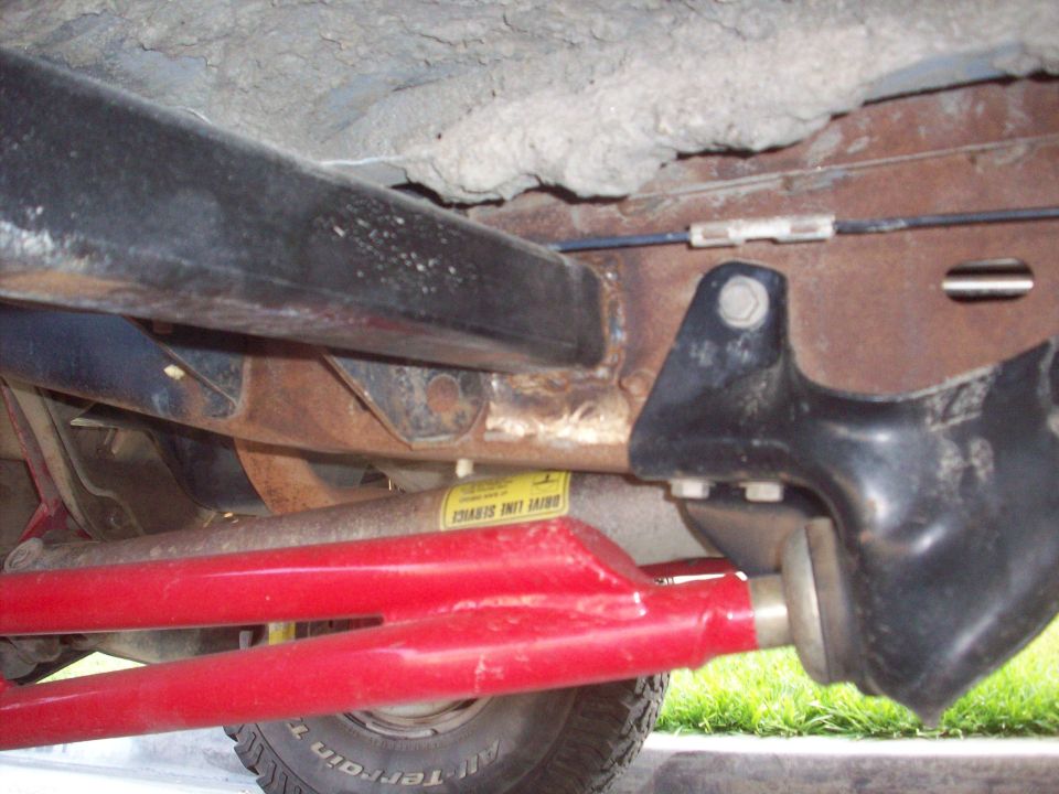 Underside of Bronco showing red suspension arms, driveshaft with yellow Drive Line Service sticker, and frame bracket
