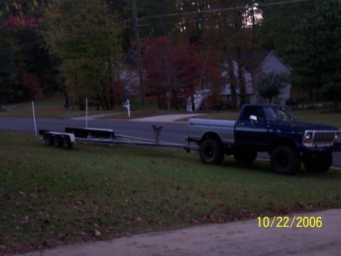 1979 Ford F-150 - A blue and silver 1979 Ford F-150 pickup truck is seen from the front-three-quarter view, towing a boat trailer on a grassy roadside.