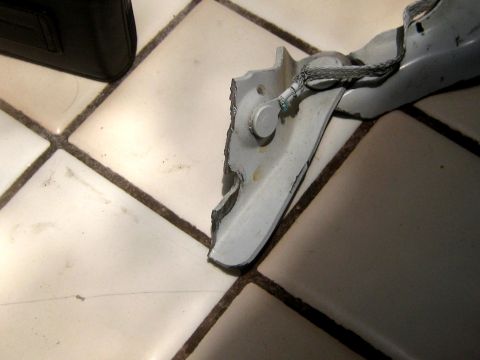 1996 Ford Bronco - A close-up view of a damaged metal bracket with a cable, lying on a tiled surface.