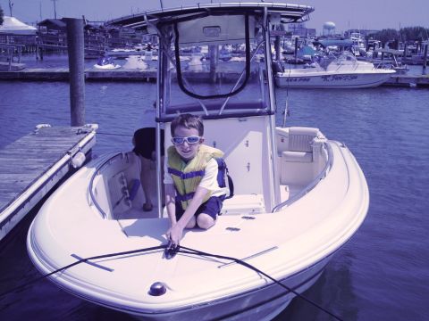 1979 Ford F-250 - A young boy wearing a life vest sits in a boat docked at a marina, with other boats visible in the background.