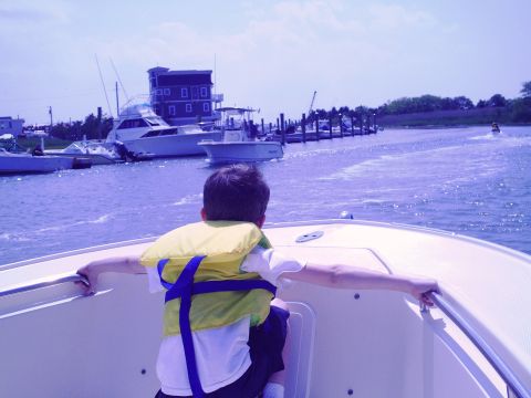 1979 Ford F-250 - A boy wearing a life jacket looks out from a boat at a marina with several other vessels docked.