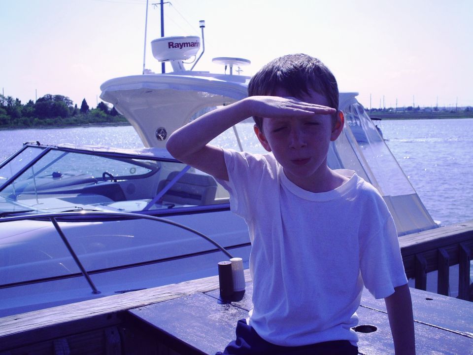 Boy shields eyes looking towards boats on the water