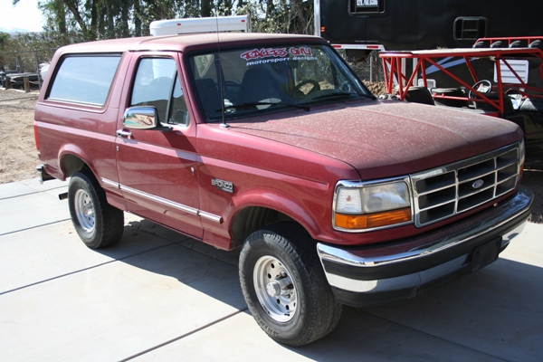 Red Ford Bronco parked outside, dust on hood. Sticker on windshield says 'EAGLE'S ON MOTORSPORT DESIGNS'