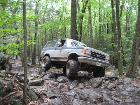 1991 Ford Bronco - This lifted Ford Bronco navigates a rocky path through a dense forest during an off-road event.