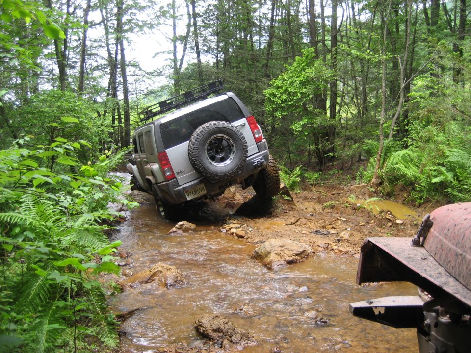 Silver SUV navigating a muddy stream, with another vehicle visible in the foreground