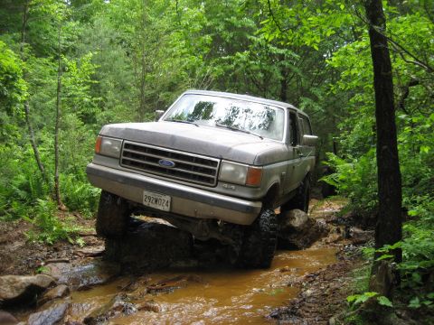 1991 Ford Bronco - 1991 Ford Bronco tackles a challenging off-road course through a wooded area.