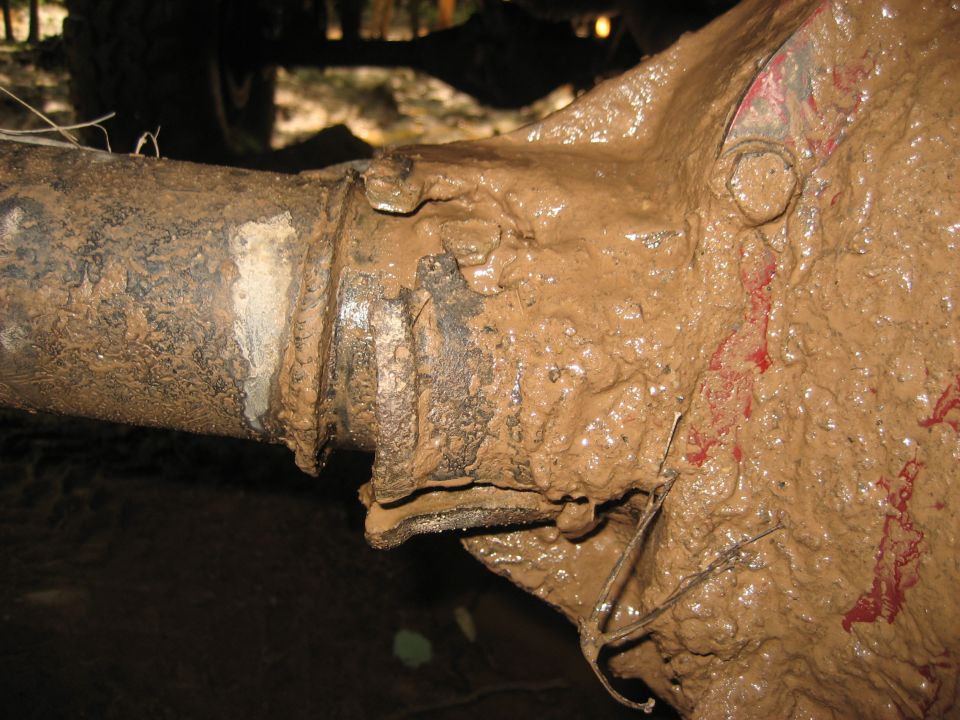 Mud-covered vehicle axle with red paint streaks and a Supermotors logo