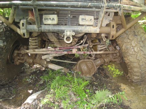 1991 Ford Bronco - Front axle and suspension of an off-road vehicle stuck in mud, showing PIAA lights.
