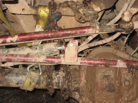 1991 Ford Bronco - Undercarriage view showing red suspension components and chains, covered in mud.