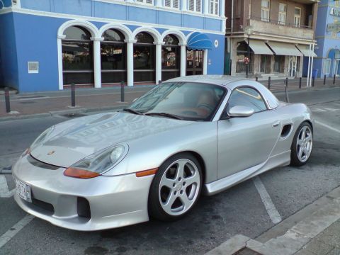 1987 Suzuki Samurai - Silver Porsche Boxster with a targa top parked on a street in front of a blue building.
