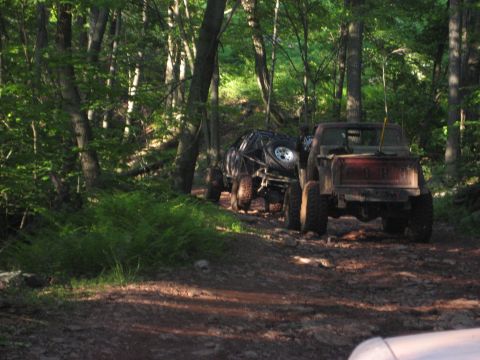 1991 Ford Bronco - Two modified off-road vehicles navigate a challenging dirt path through a wooded area.