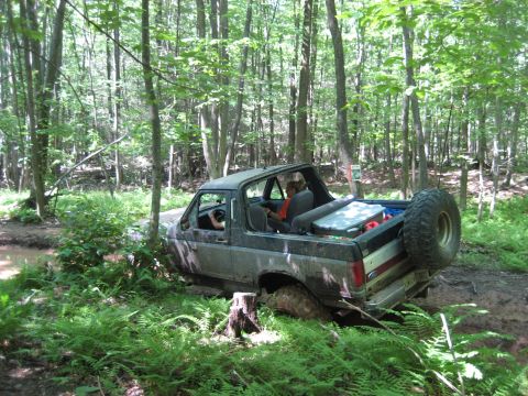 1991 Ford Bronco - Ford Bronco navigating a muddy trail surrounded by dense forest foliage.