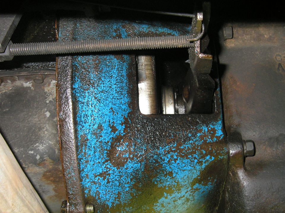Close-up of a greasy blue metal part with a spring and linkage mechanism