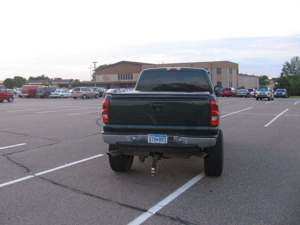 Rear view of a lifted dark green pickup in a parking lot
