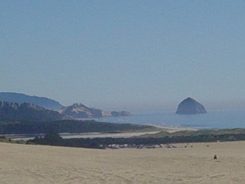 1989 Ford Bronco - A wide view of a coastal landscape sand dunes, vegetation, and a prominent rock formation in the ocean under a clear sky.